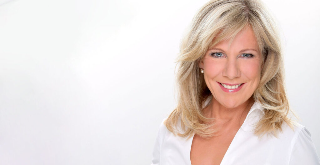 Moderatorin Ulrike von der Groeben in weißer Bluse vor hellem Hintergrund